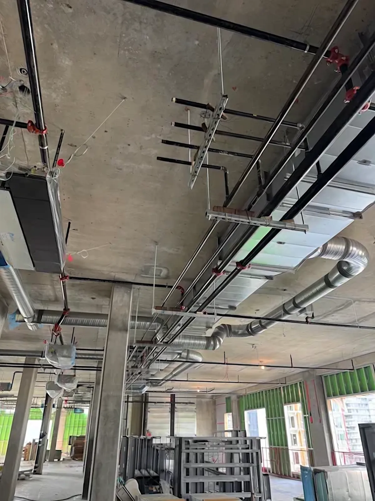 Commercial main supply ductwork and spiral duct running alongside VAV piping on an open concrete office floor