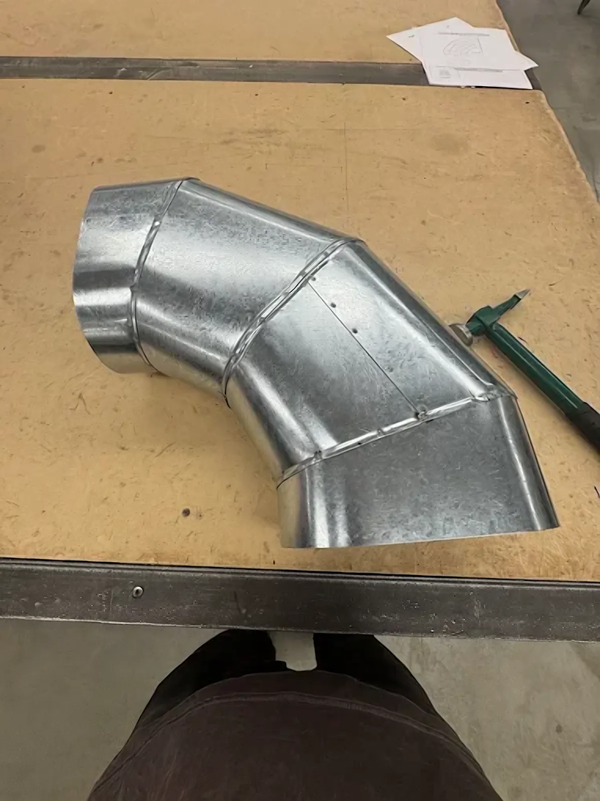 Custom oblong elbow HVAC fabrication – hand-built galvanized gored elbow on a shop bench